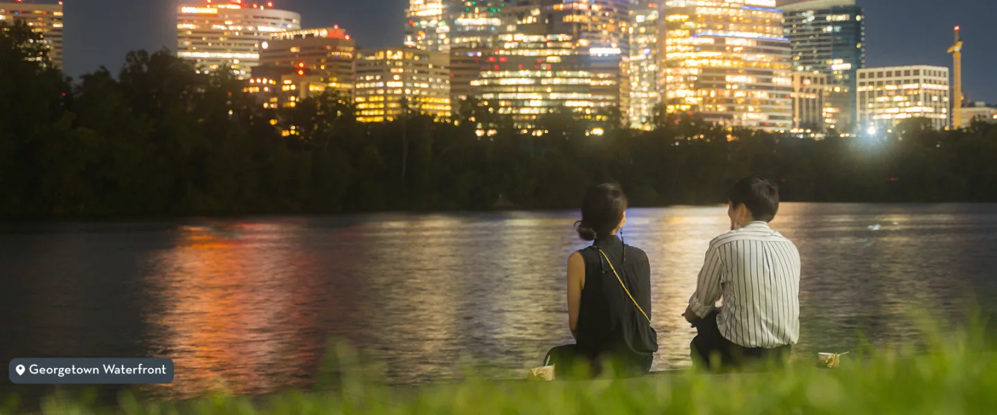 Two people sitting along the Georgetown waterfront at night