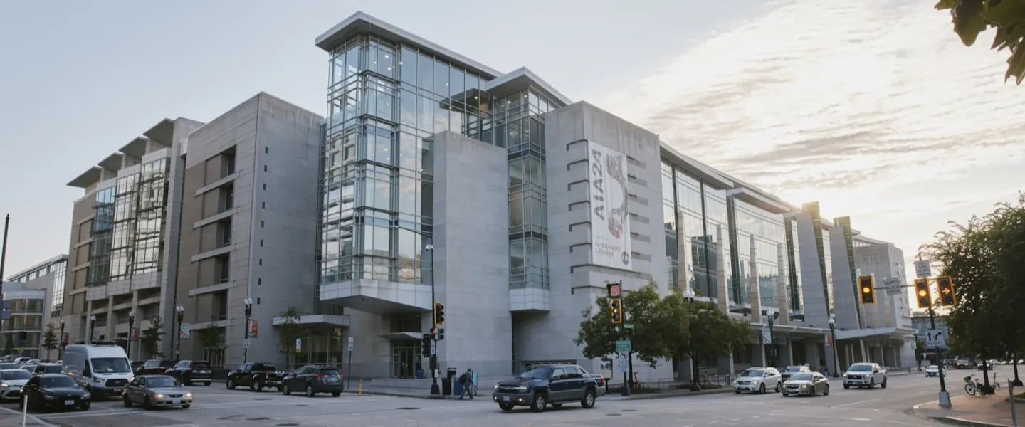A modern glass-and-concrete museum building on a city corner with cars and pedestrians under a partly cloudy sky.