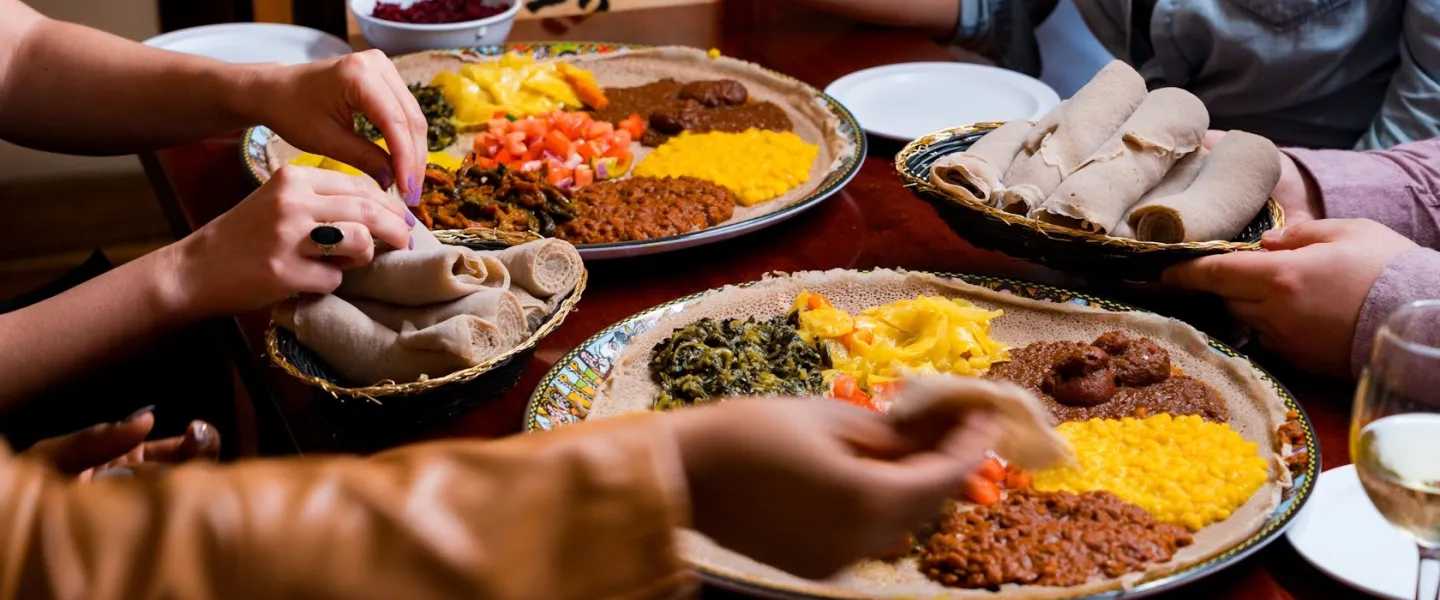 Hands sharing Ethiopian injera platter with stews