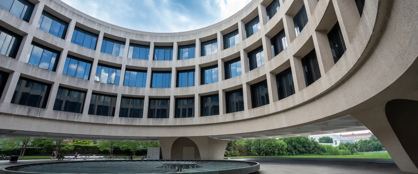 Curved modern building with large windows surrounding a circular fountain under blue sky