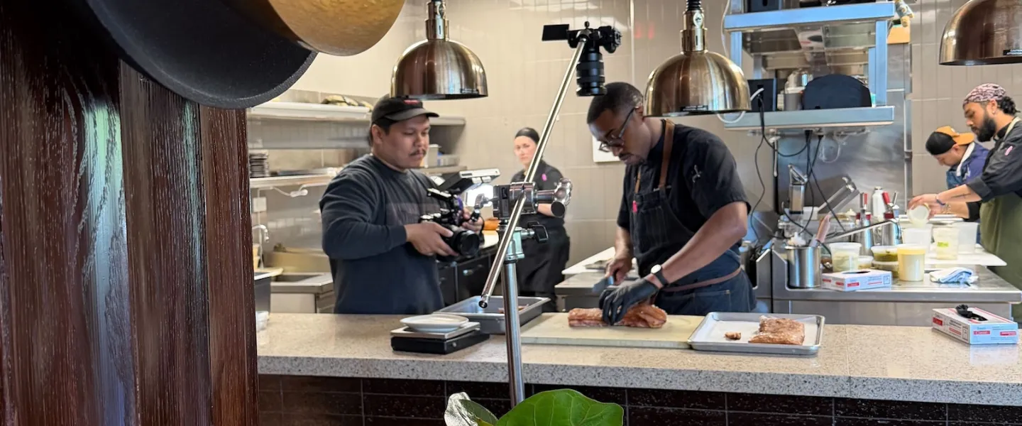 A videographer filming a chef in a professional kitchen with cameras and lights