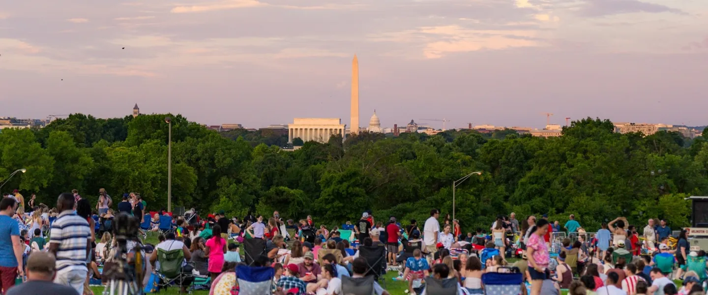 Crowd picnicking at sunset with the Washington Monument in the distance