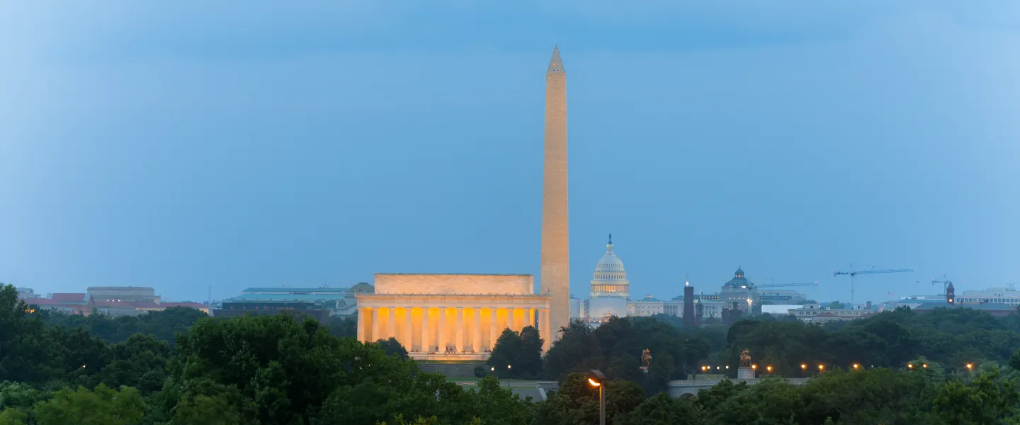 Washington Monument and illuminated Lincoln Memorial at dusk, seen over trees