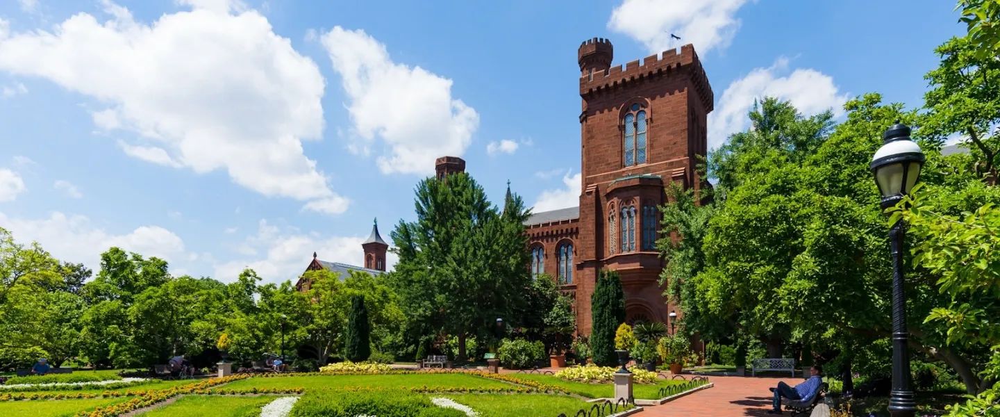 Brick building behind a green lawn and trees under a blue sky