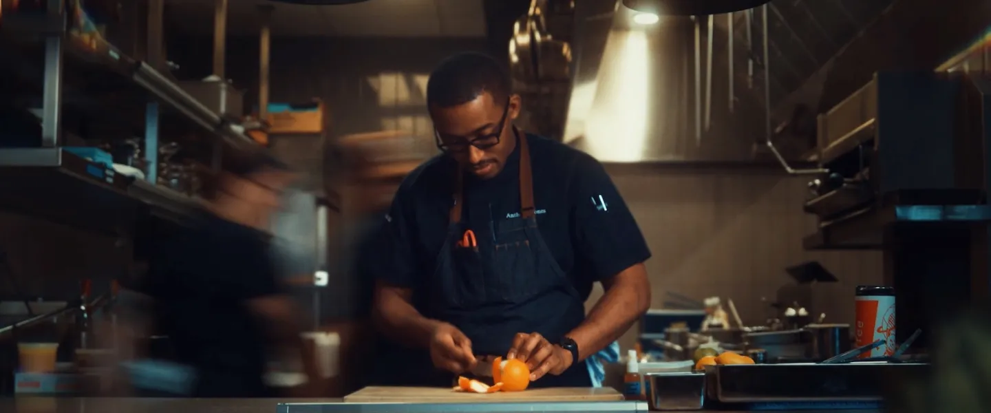 Chef slicing vegetables at a stainless-steel kitchen counter, with motion blur around him