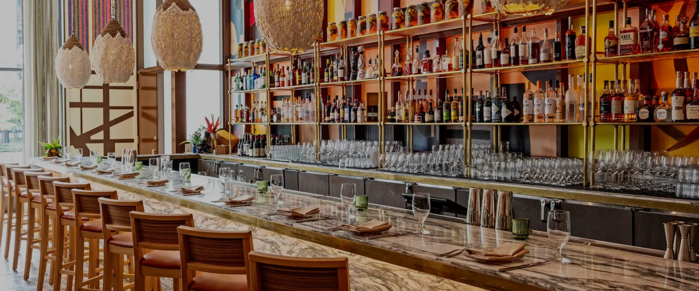 Long wooden bar with colorful decor, stools and shelves of liquor bottles behind it