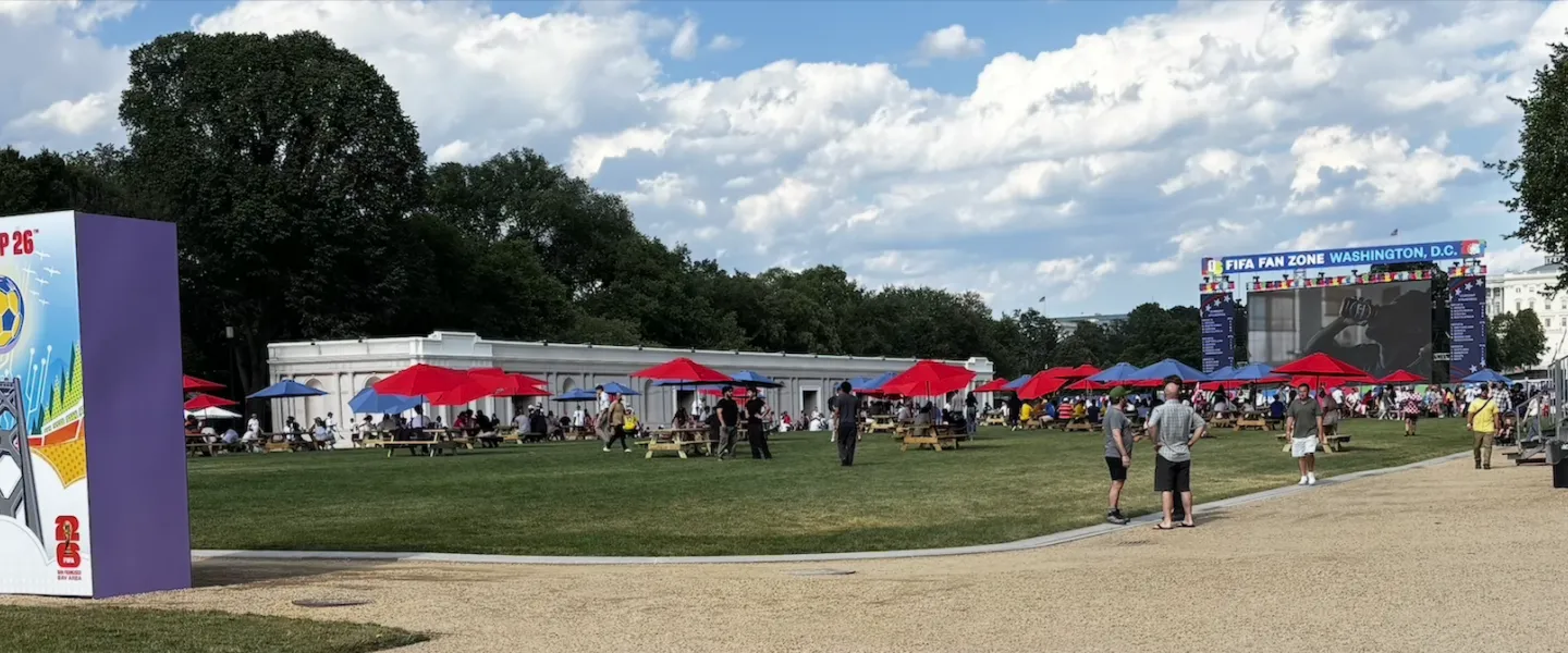 Outdoor festival on the National Mall with tents, a large screen and people under a cloudy sky