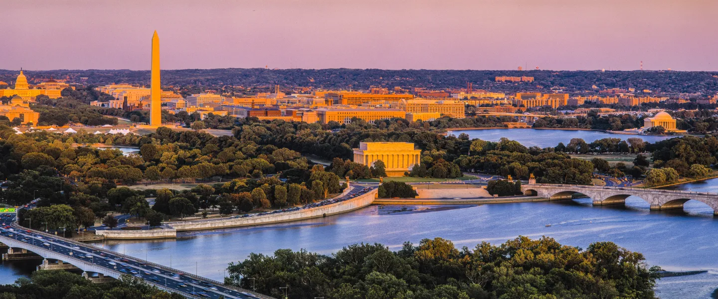 Panoramic view of a riverside city at sunset, with bridges and a tall monument.
