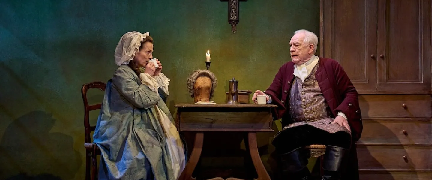 Two people seated at a table on a stage in historical dress