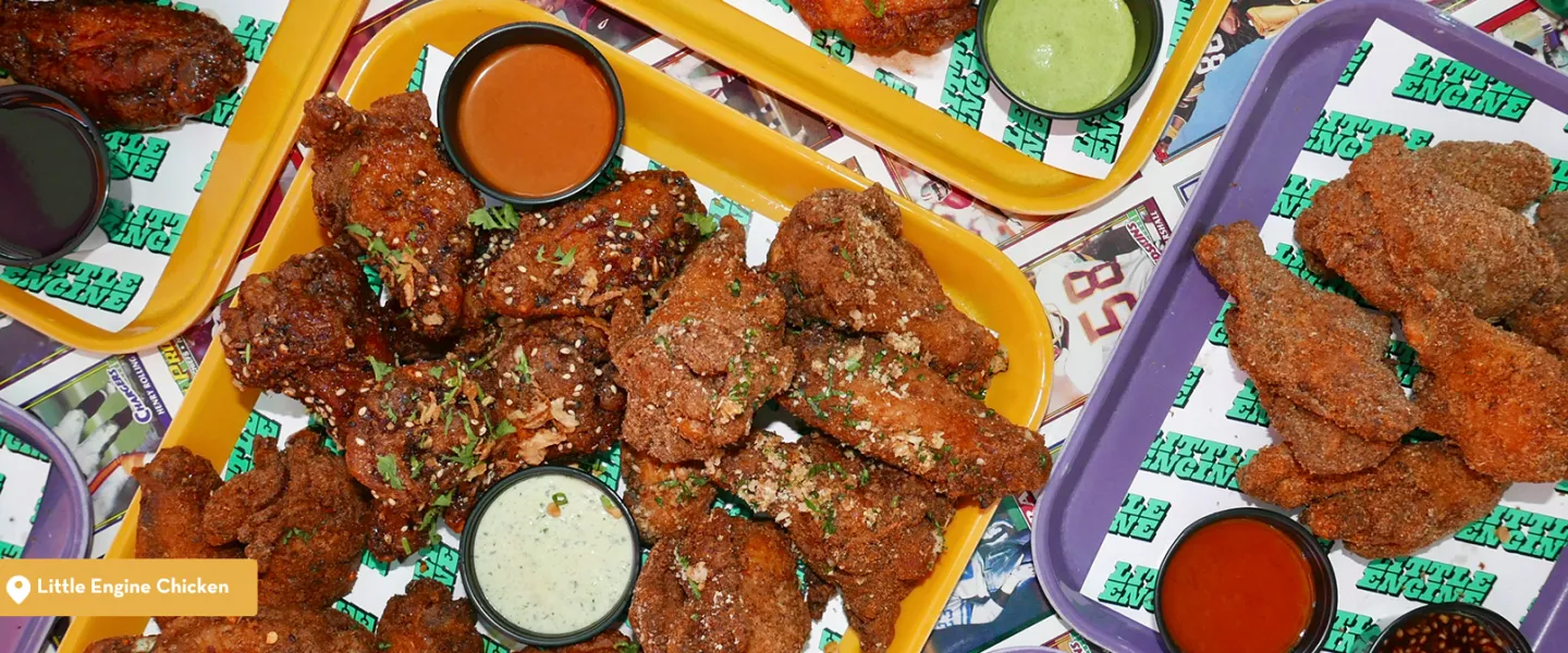 Platters of sauced wings, fried chicken tenders and dipping sauces on a colorful table