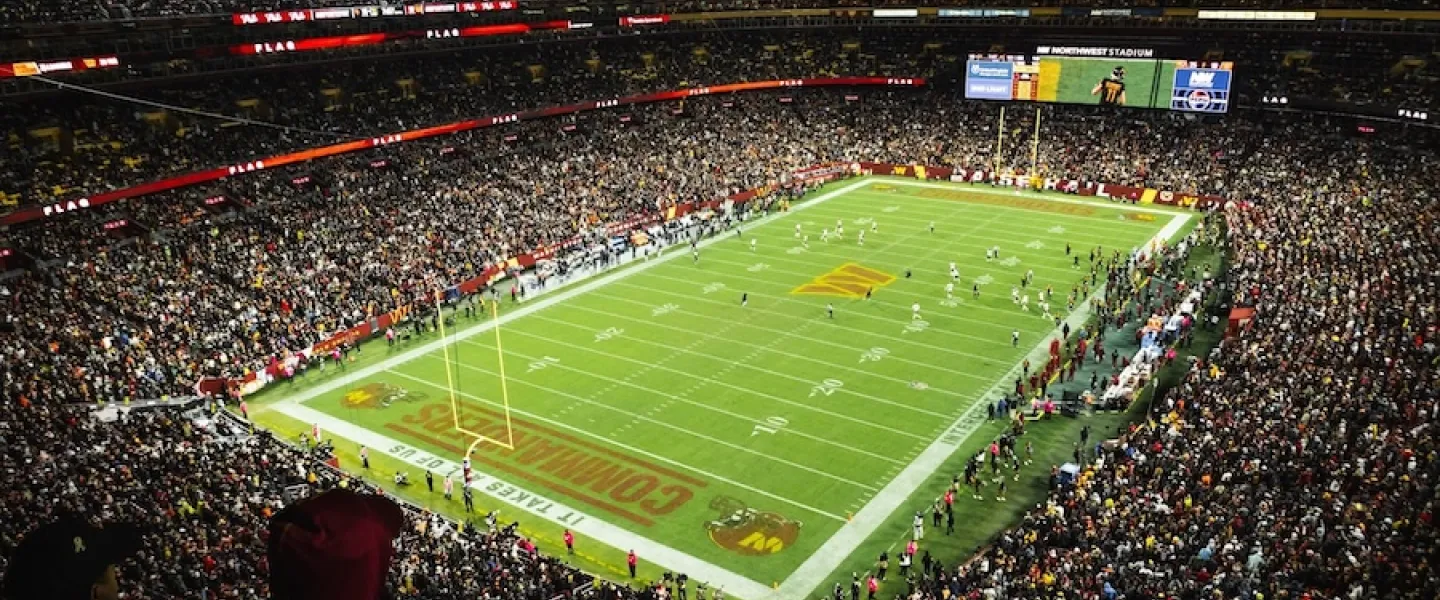 Packed football stadium at night, bright green field under lights