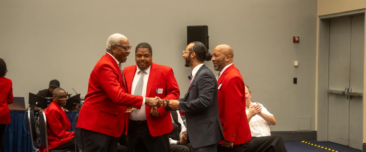 People in red blazers greet and chat in a conference room.