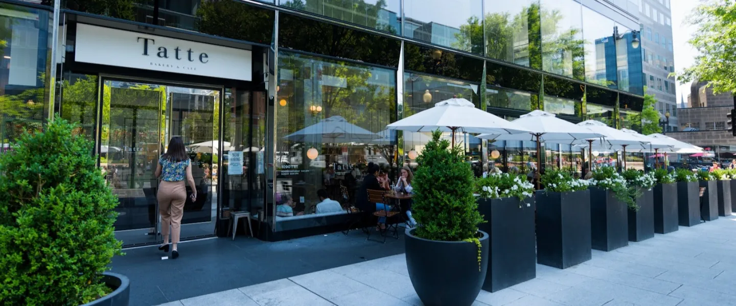 Sidewalk cafe with white umbrellas and diners outside a glass-front restaurant
