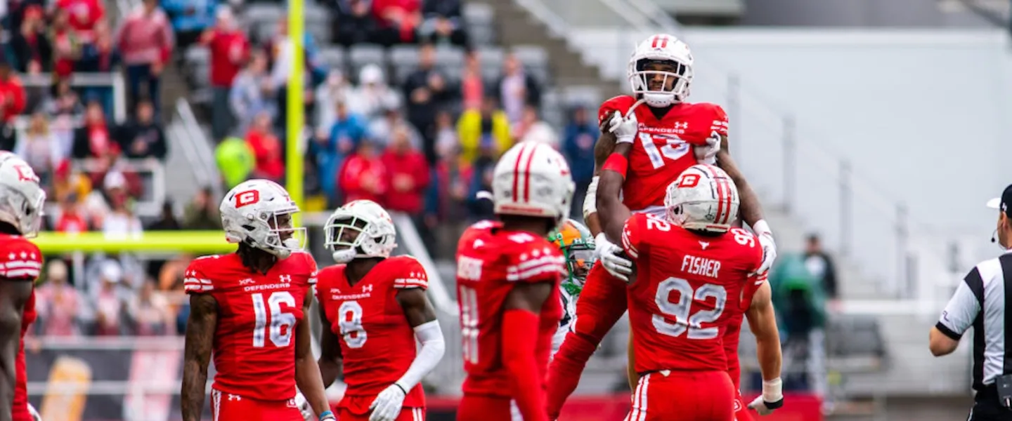 Photo, football players in red uniforms celebrate on the field as crowd watches.
