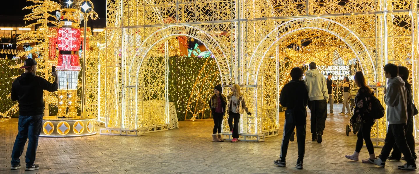 Photo: People walking past large golden holiday light arch at night