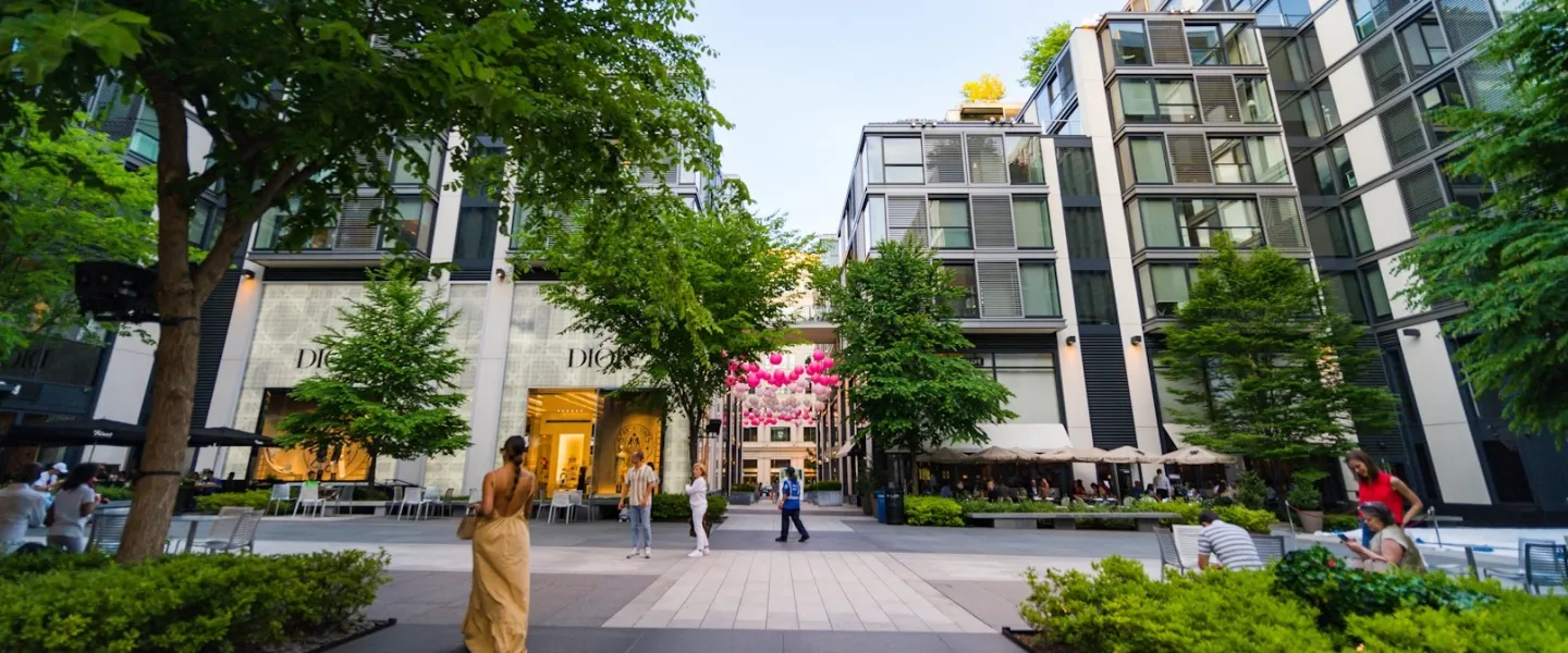 Modern glass building on tree-lined street with pedestrians and storefronts