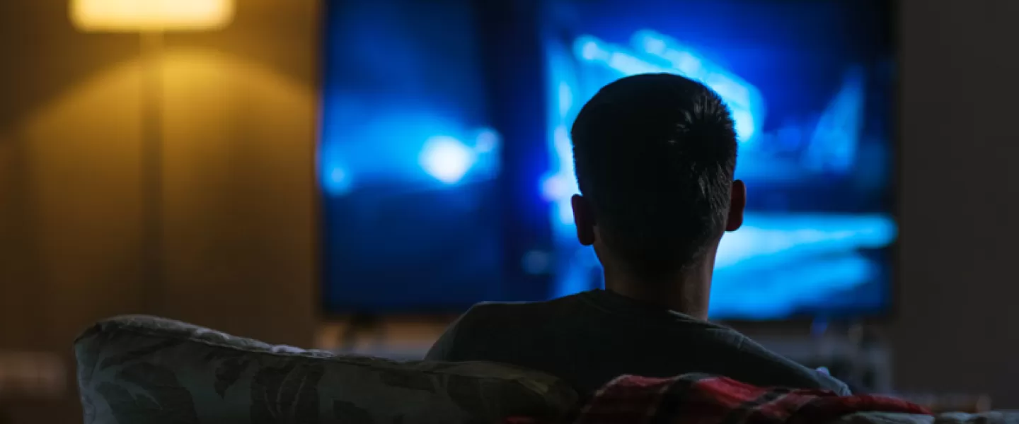 boy facing the television watching it in the dark