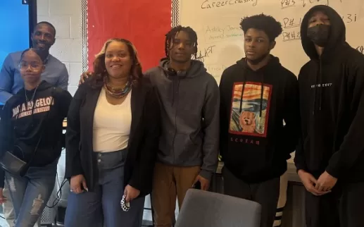 Uma profissional negra sorri e fica com um grupo de estudantes negros do ensino médio na Maya Angelou Public Charter School.