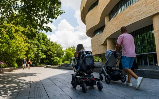박물관 밖에 있는 가족, 한 가족은 유모차를 밀고 있고 다른 한 가족은 휠체어를 타고 있습니다.