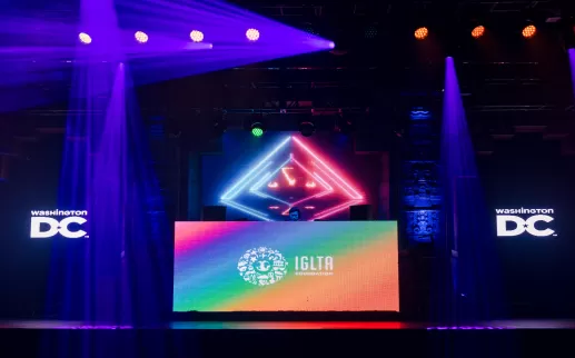 A colorful stage setup with vibrant lighting and LED screens displays logos for Washington D.C. and the IGLTA Foundation.
