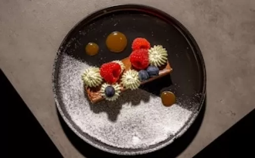 A visually appealing dessert plate with colorful garnishes including raspberries and blueberries, artistically arranged with a light dusting of powdered sugar.
