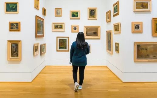 Un visitatore esplora una galleria della Phillips Collection, dove piccoli dipinti incorniciati in vari stili sono disposti su pareti bianche, creando un'esperienza artistica immersiva.