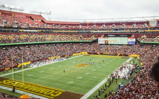A packed stadium during a Washington Commanders football game, with fans filling the stands and players on the field at FedExField.