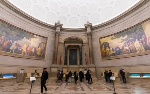 Visitors explore the Rotunda for the Charters of Freedom at the National Archives in Washington, DC, surrounded by murals and historical displays.