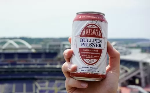 Una mano sostiene una lata de cerveza con una vista del Nationals Park en el fondo.
