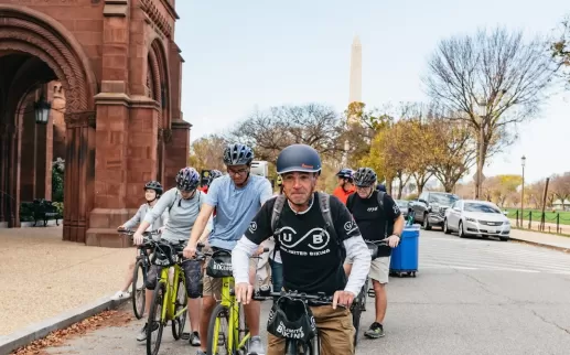 Un guía dirige un recorrido en bicicleta por el National Mall con el Castillo Smithsonian y el Monumento a Washington al fondo.