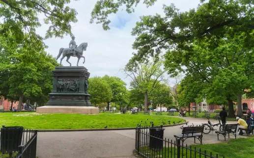 Szeroki widok na Logan Circle Park z dużą statuą konną otoczoną drzewami liściastymi i ławkami w słoneczny dzień.