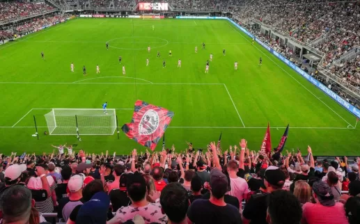 A soccer stadium is packed with fans in red and black at a night game. 