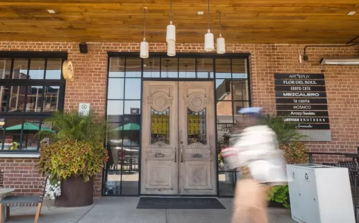 The exterior of La Cosecha, with an ornate wooden door, plants, hanging lights, and furniture outside. 