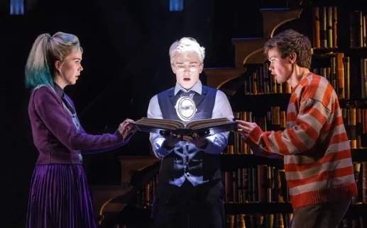 Three characters intensely examine a glowing magical object in a dramatic scene from Harry Potter and the Cursed Child.
