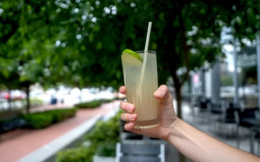  A hand holds out a refreshing green cocktail with lime. 

