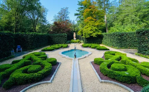 Formal garden with sculpted boxwood hedges, a central fountain, and a classical statue surrounded by tall green hedges in Washington, DC.

