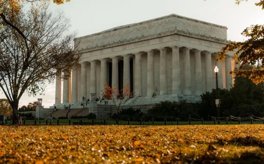The Lincoln Memorial framed by fall foliage, with leaves coverage the grass in orange and yellow hues.