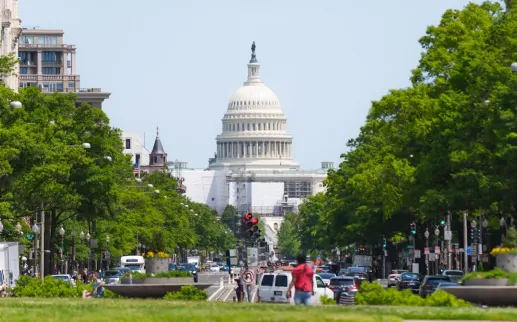 A wide view of Pennsylvania Avenue, lined by trees and leading toward the U.S. Capitol Building.

