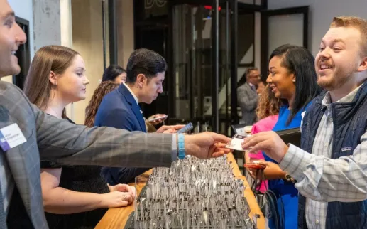A man smiles as he receives a name badge at an event check-in table staffed by several people.