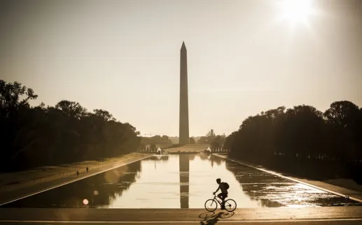 A cyclist rides past the Reflecting Pool with the Washington Monument rising in the background at sunrise.