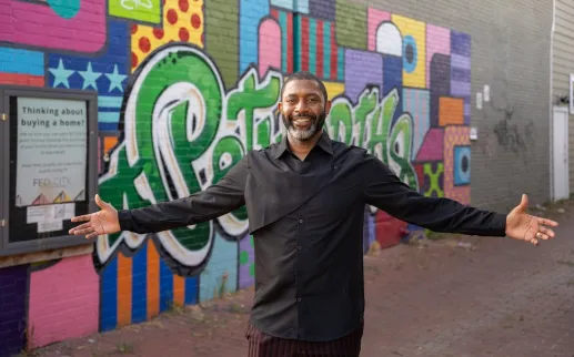 A smiling man stands with his arms open in front of a colorful street mural in Washington, DC.
