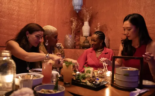 À Washington, D.C., un groupe d'amis partage des tapas et des cocktails colorés au restaurant Doi Moi, assis autour d'une table éclairée à la bougie, avec des murs aux textures chaleureuses en arrière-plan.