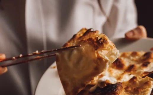 A hand uses chopsticks to lift some crispy, oven-fired bread off of a plate.
