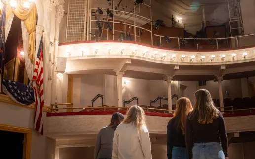 A group of people stand on stage, looking up into the box seating section of the historic Ford's Theatre.