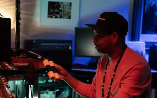 A DJ adjusts equipment in a dimly lit home studio with colorful lighting.
