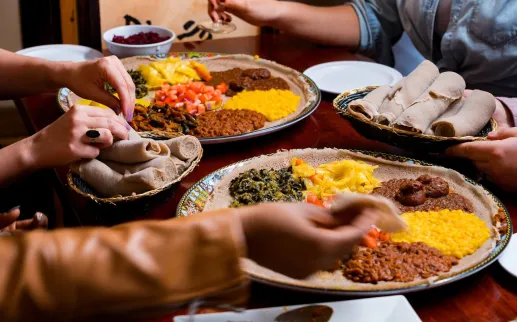 Hands sharing Ethiopian injera platter with stews
