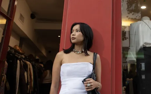Woman in strapless white top standing by red doorway, looking left
