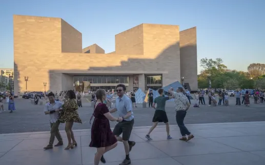 People walking in a plaza outside a modern beige stone building at dusk
