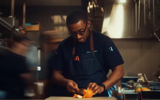 Chef in a dim kitchen preparing food under warm task lighting
