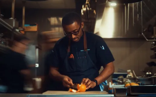 Chef slicing vegetables at a stainless-steel kitchen counter, with motion blur around him